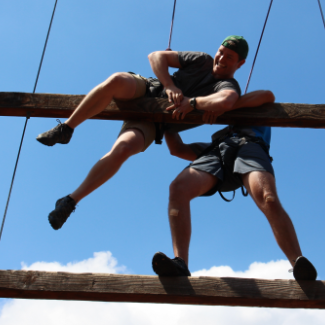 man helping another man over a log in the uc riverside ropes course